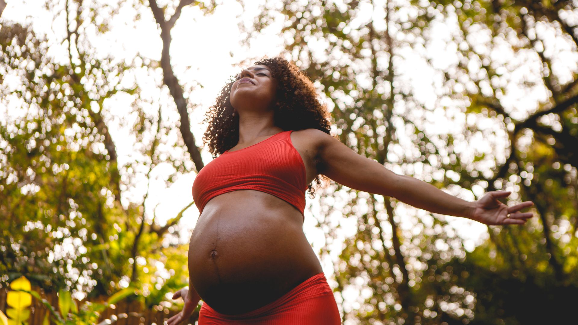 A pregnant woman in a red bikini top is standing in the woods